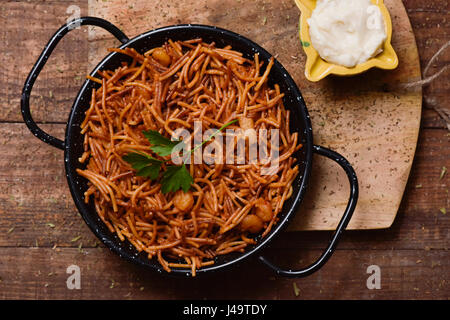 Alta angolazione di una fideua spagnola, un tipico tagliatelle casseruola con frutti di mare, in una padella per paella e salsa aioli in un mortaio di giallo su un legno rustico t Foto Stock