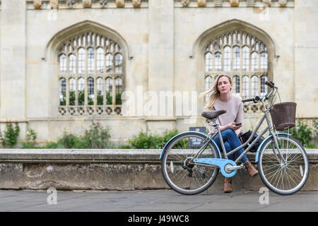 Triste studente con la sua bicicletta si siede su un muro basso nella parte anteriore del King's College dell'università di Cambridge, Inghilterra, Gran Bretagna. Foto Stock