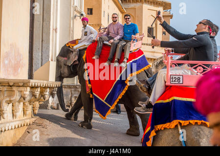 I turisti sorriso come essi cavalcare un elefante fino a Forte Amer a Jaipur, India. Foto Stock