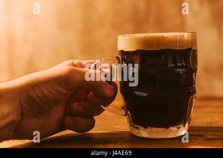 Uomo di bere birra scura in british puntinati pinta di birra in vetro mug sul tavolo bar Foto Stock