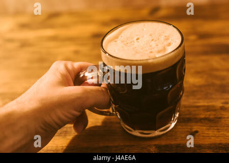 Uomo di bere birra scura in british puntinati pinta di birra in vetro mug sul tavolo bar Foto Stock