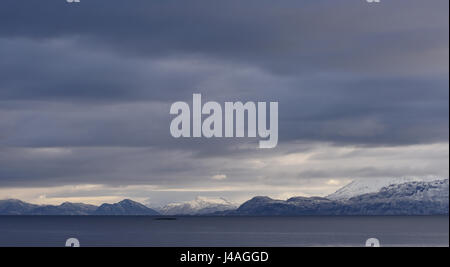 Un cupo, nuvoloso, grigio cielo invernale sopra il mare e le isole nevoso vicino a Harstad. Harstad, Troms, Norvegia. Foto Stock