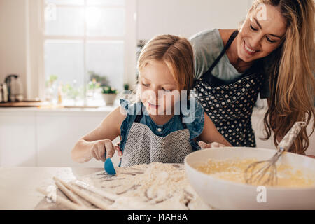 Colpo di bambina aggiungendo farina per la pastella in una terrina. Madre insegnare a sua figlia di cucinare nella cucina di casa. Foto Stock