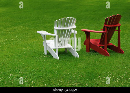 Rosso e bianco sedie Adirondack su un vasto prato. Foto Stock