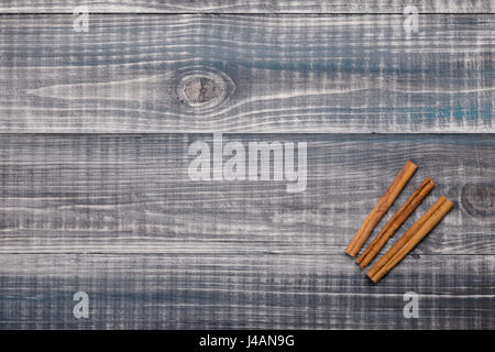 Grigio sfondo di legno con tre bastoncini di cannella giacente su di esso. Vista dall'alto. Spazio libero. Foto Stock