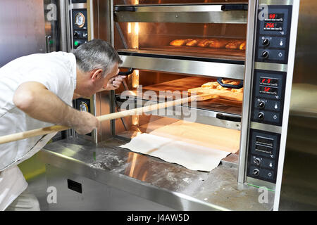 Baker cuoce il pane nel forno Foto Stock