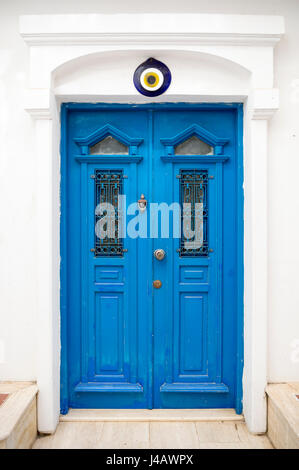 Tradizionale blu del Mediterraneo e la porta bianca con un bagno turco di cattivo occhio protezione 'nazar' medaglione sulla parte superiore del vano porta Foto Stock