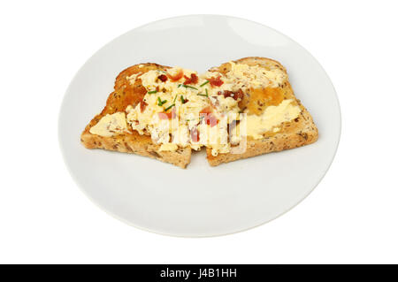 Uova strapazzate con croccante di prosciutto e erba cipollina integrale sul pane tostato, su una piastra isolata contro bianco Foto Stock