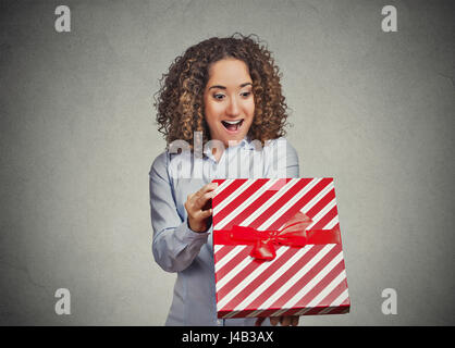 Closeup ritratto felice super eccitati giovane donna apertura rosso di unwrapping regalo di compleanno box, isolato muro grigio Sfondo. Positive le emozioni umane, fac Foto Stock