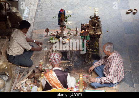 Tre uomini facendo Offerte e preghiere per il Buddha il compleanno nel Tempio d'Oro - Hiranyavarna Mahavihara - Patan, o Lalitpur, Kathmandu, Nepal Foto Stock