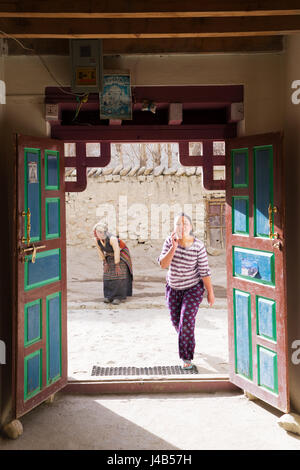 Tibetano ragazza adolescente parlando al cellulare e la donna più anziana vestito in abiti tradizionali in background. Foto Stock