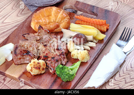 Home realizzato ,bistecca di carne di maiale con la carota tagliata a fette, fungo, mais , broccoli ,cipolla e croissant su butcher servito. Foto Stock