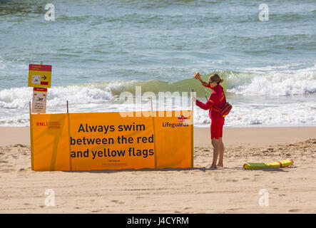 Femmina bagnino RNLI mettendo banner di sicurezza sempre nuotare tra il giallo e il rosso bandiere a Bournemouth Beach nel Maggio Foto Stock