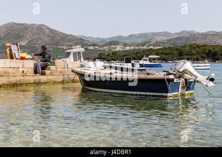 Un pescatore descales & coraggio il suo pescato del pesce sulla banchina del porto di Kolocep. Foto Stock