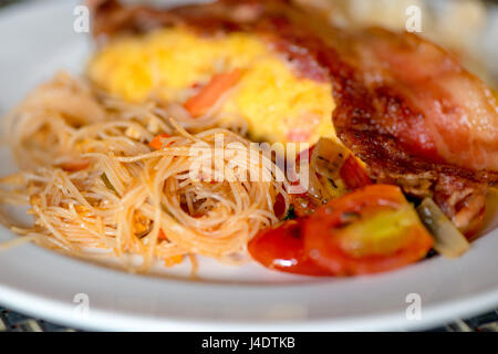 Piatto asiatico - noodles fritti con uova, pomodori e pancetta close-up su una piastra Foto Stock