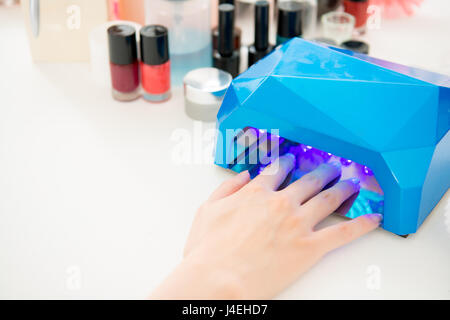 Close up della splendida giovane donna convincendola chiodi fatto da un manicurist portatile con luce UV essiccatore e manicure gli oggetti correlati in un salone di bellezza. Foto Stock