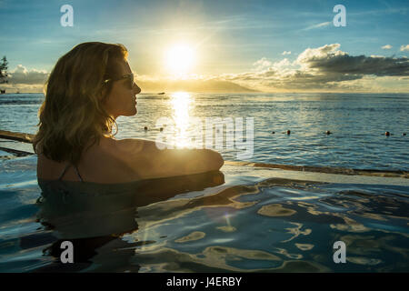 Donna godendo del tramonto in una piscina con Moorea in background, Papeete, Tahiti, Isole della Società Foto Stock