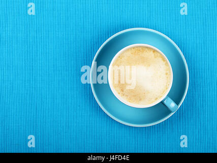 Piena tazza di cappuccino cappuccino con schiuma di latte sul piattino sulla tovaglia blu, close up, elevati vista superiore Foto Stock