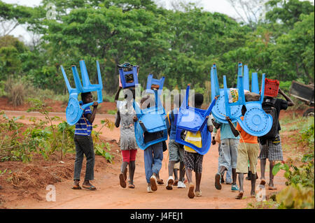 ANGOLA, Kwanza Sul, villaggio Kassombo, i bambini sulla strada per la scuola, ogni bambino deve portare la propria sedia in plastica come le scuole in cattivo stato a causa della guerra civile e la corruzione, i ricavi da olio ricco Angola sembra non raggiungere i villaggi / ANGOLA Kwanza Sul, Dorf Kassombo, Kinder mit Plastikstuehlen auf dem Weg zur Schule durch Felder des Dorfes, da die Schulen durch den Buergerkrieg zerstoert und ohne Inventar sind, muss jedes tipo seinen Plastik Stuhl mitbringen Foto Stock