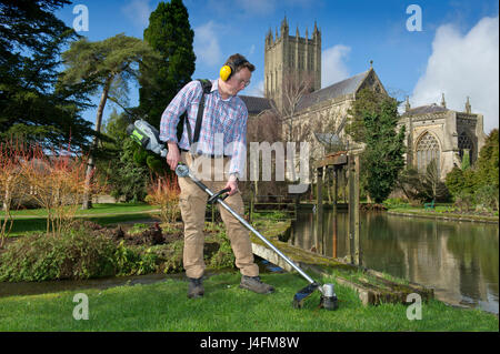 James cross, il capo giardiniere il taglio dell'erba nel palazzo del vescovo della Cattedrale di Wells (edificio in background) Foto Stock