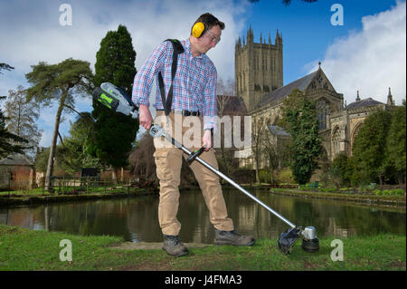 James cross, il capo giardiniere il taglio dell'erba nel palazzo del vescovo della Cattedrale di Wells (edificio in background) Foto Stock