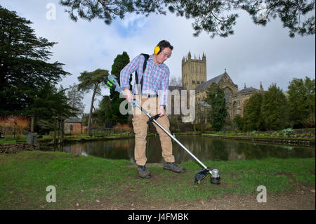 James cross, il capo giardiniere il taglio dell'erba nel palazzo del vescovo della Cattedrale di Wells (edificio in background) Foto Stock