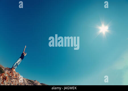 Giovane uomo in jeans e maglietta nera su una montagna sollevate le mani al cielo verso il sole. Il concetto di viaggio photo. Foto Stock