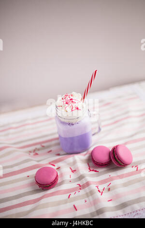 Caffè viola in stilizzata mason jar cup con macarons e rose e decor colorato. Mirtillo milk shake. Unicorn caffè. Unicorn cibo Foto Stock