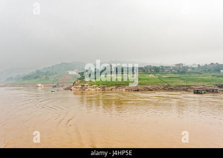 Case galleggianti ormeggiate sulle ripide sponde del fiume Yangtze, nei pressi di una piccola città sul fiume. La nebbia si raccoglie nelle lontane colline. Foto Stock