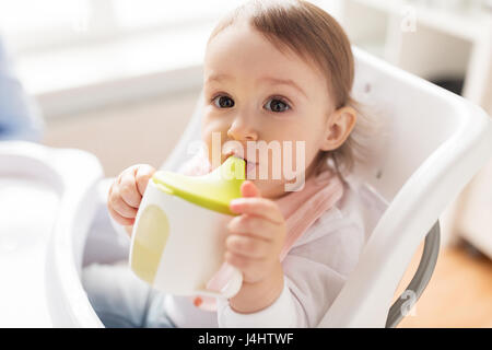 Baby bere dal bicchiere del tubo di lancio nel seggiolone a casa Foto Stock