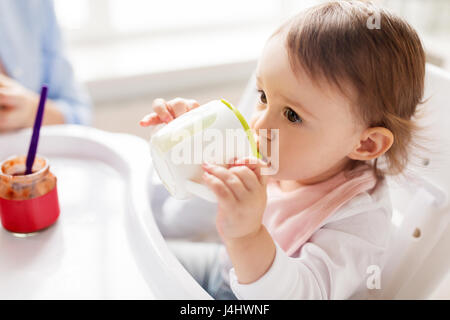 Baby bere dal bicchiere del tubo di lancio nel seggiolone a casa Foto Stock