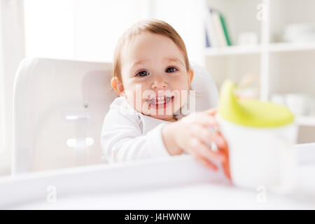 Baby bere dal bicchiere del tubo di lancio nel seggiolone a casa Foto Stock