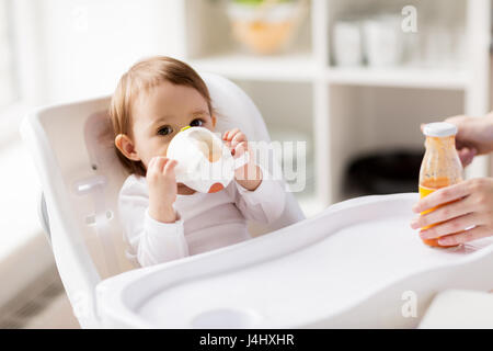 Baby bere dal bicchiere del tubo di lancio nel seggiolone a casa Foto Stock