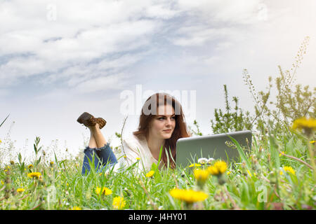 Redhead donna utilizzando laptop nel parco sdraiati sull'erba verde. Foto Stock