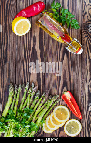 Bottiglia di olio di oliva con spezie, mazzo di freschi Asparagi verdi lance e limone su una tavola in legno rustico Foto Stock