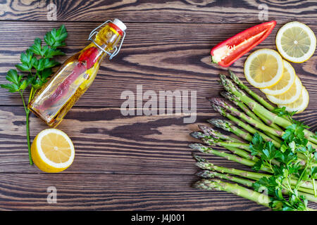 Bottiglia di olio di oliva con spezie, mazzo di freschi Asparagi verdi lance e limone su una tavola in legno rustico Foto Stock