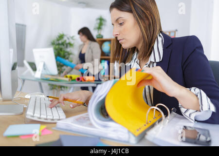 Giovane imprenditrice guardando attraverso una pila di cartelle di file Foto Stock