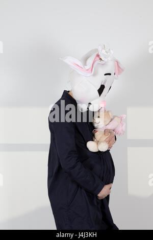 Donna incinta coniglio toccando e guardando il suo ventre gestante coniglio oscillando un orsacchiotto Foto Stock