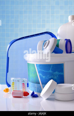 Ai prodotti chimici di pulizia per acqua di piscina sul tavolo bianco e blu sullo sfondo di mosaico. Composizione verticale. Vista frontale Foto Stock