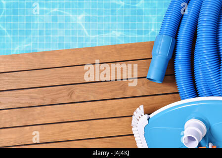 Strumenti per la manutenzione della piscina su assicelle di legno. Con piscina con acqua e mosaici blu sullo sfondo. Composizione orizzontale. Vista superiore Foto Stock