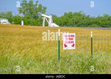 Un sistema elettronico di sorveglianza protegge un martinetto della pompa con serbatoio batteria dietro la maturazione di un campo di grano in Oklahoma, Stati Uniti d'America. Foto Stock