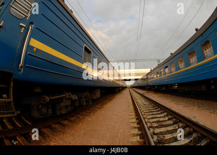 Due treni con vagoni blu e tra di loro e rotaie, convergono in un punto all'orizzonte. Foto Stock