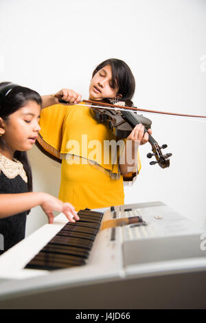 concetto di musica e bambini - le bambine indiane che suonano strumenti musicali come pianoforte, tastiera o violino Foto Stock