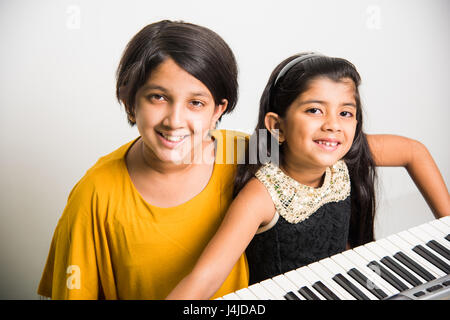 Due carine bambine indiane/asiatiche suonano pianoforte o tastiera, uno strumento musicale, su sfondo bianco Foto Stock