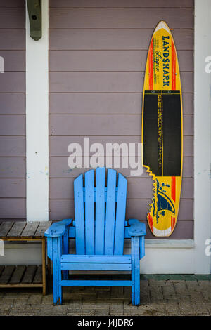 Blu brillante Adirondack sedia accanto ad una tavola da surf con la pubblicità per Landshark recare in un piccolo centro commerciale vicino Grayton beach florida, Stati Uniti d'America. Foto Stock