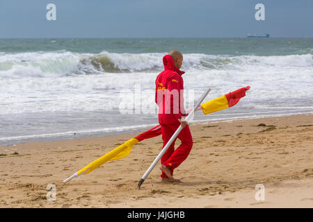 Bagnino RNLI portante il rosso e il giallo di flag che indicano una zona sicura per nuotare al mare sulla spiaggia di Bournemouth Dorset, nel mese di aprile Foto Stock