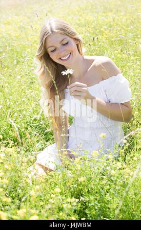 Giovane donna seduta in prato azienda daisy. Foto Stock