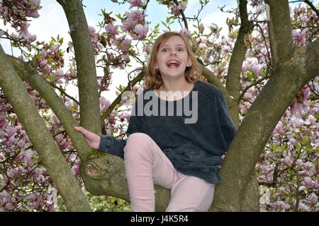 Giovane ragazza si siede in un albero di magnolia e risate in avanti Foto Stock