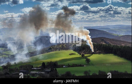 Fumo di combustione sopra i registri di paesaggio collinare in Galles Foto Stock