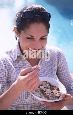 Margine di piscina, donna, giovane, hanno la colazione, mangiare cornflakes, ritratto di donna ritratto, con i capelli lunghi, attraente, tempo libero, vacanze, ora del giorno, mattino, estate, all'esterno, lifestyle, prima colazione, la nutrizione sana, felicemente, sorriso, sfondo, piscina, le sfocature Foto Stock